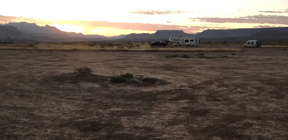 The sun, rising over some mesas and rock formations.